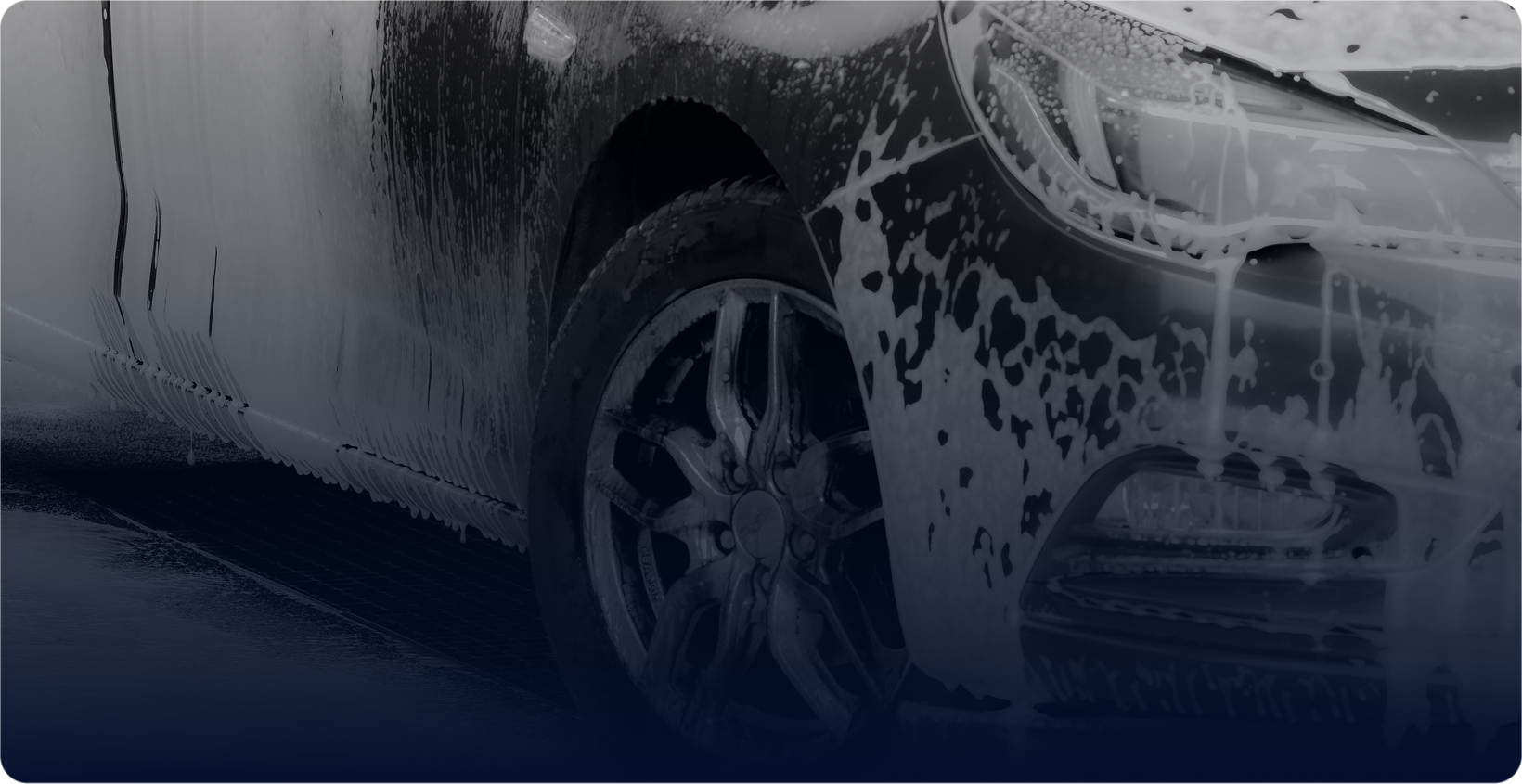 A dark car covered in foam going through a wash